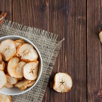 Some dried apples with dry cinnamon in a bowl on cloth and wooden background, top view.